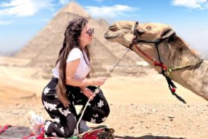a woman kneeling next to a camel in Giza Pyramids
